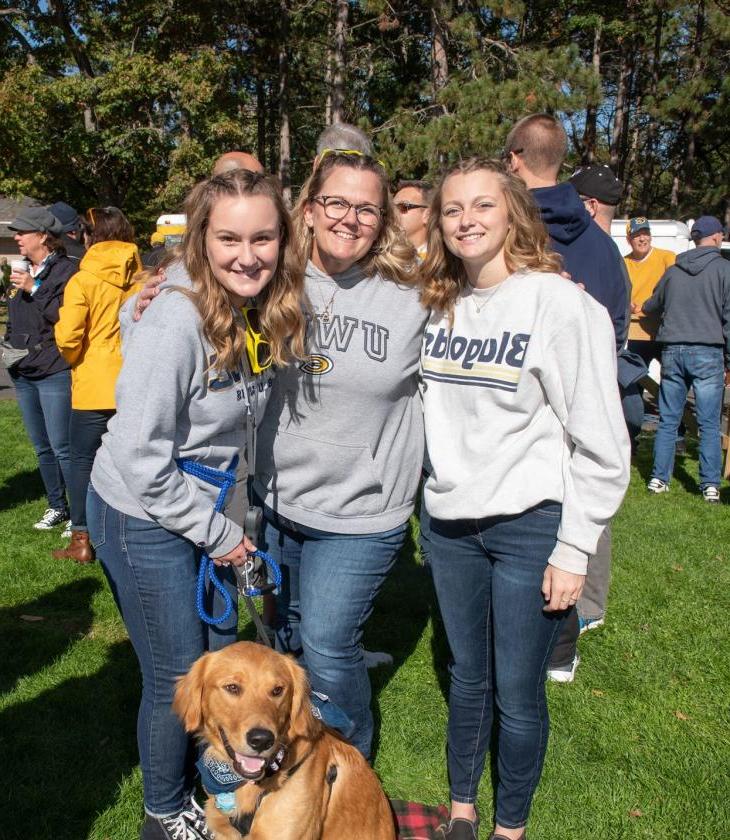 Three alumni in Blugold sweatshirts with a dog.